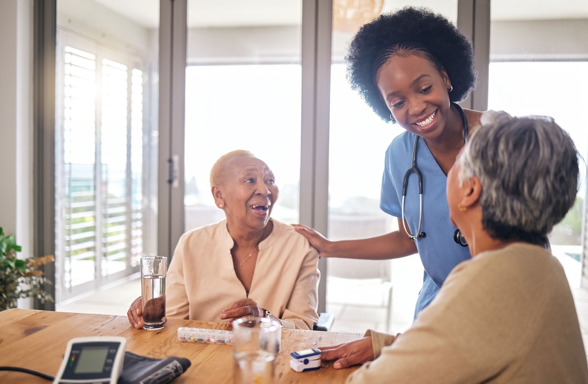 Doctor with senior women at table in nursing home for consultation, check up and conversation. Nurse, caregiver or medical professional with elderly patient in living room for advice, chat and care